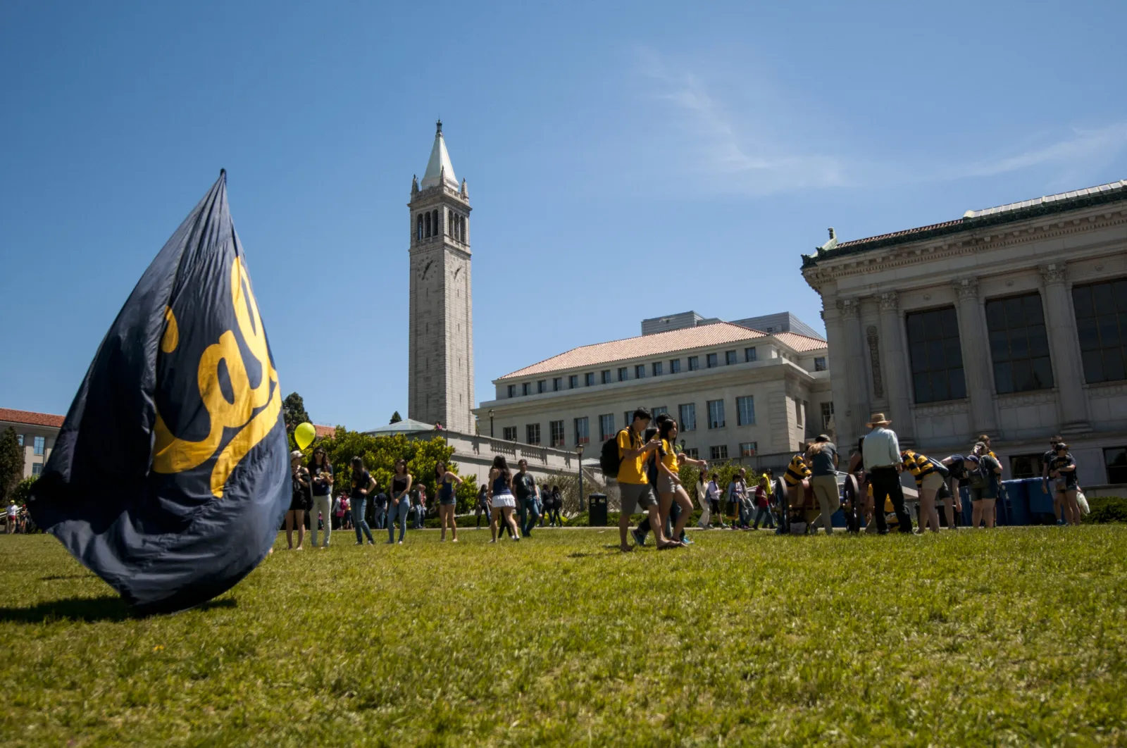 Sather Tower and a Cal flag on the UC Berkeley lawn, with students gathered on a sunny day