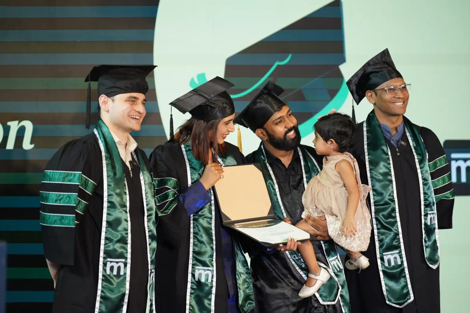 Four Mesa School of Business graduates in caps and gowns holding a certificate